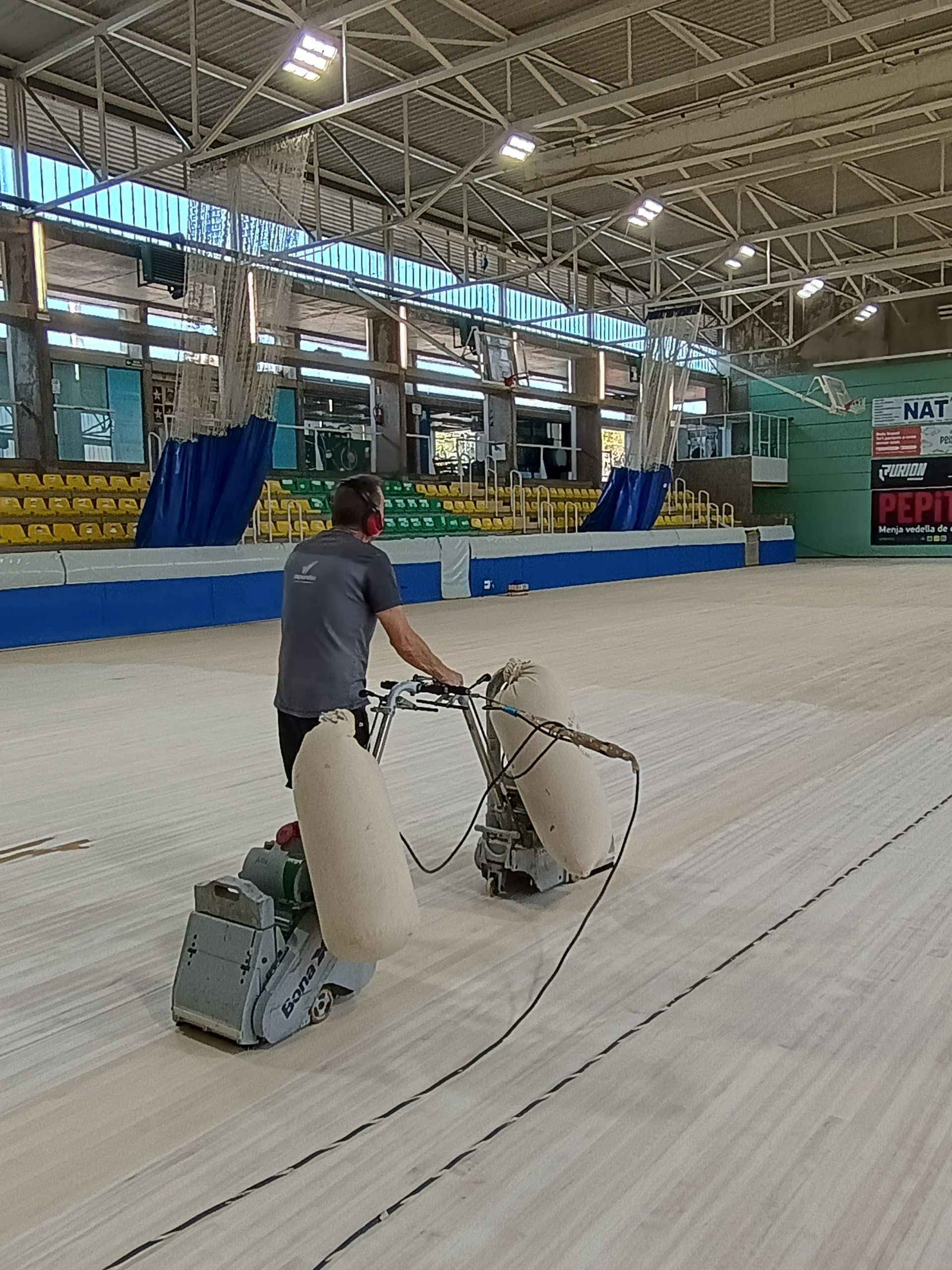 Operari polint el parquet de la pista interior d’un pavelló esportiu